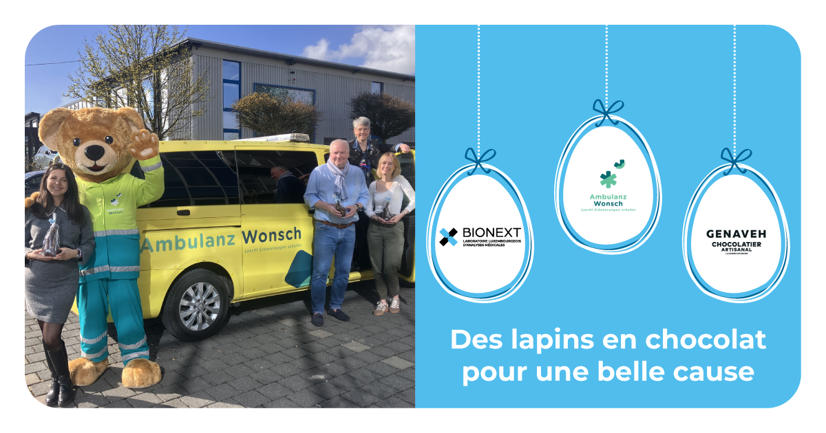 Devant un véhicule jaune d’Ambulanz Wonsch, quatre adultes et une mascotte en costume d’ours souriant posent ensemble en extérieur, chacun tenant un lapin en chocolat. À droite, un visuel graphique présente les logos de BIONEXT, Ambulanz Wonsch et Genaveh, avec le message : ‘Des lapins en chocolat pour une belle cause