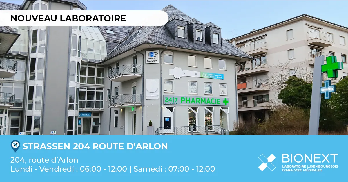 Façade d’un nouveau laboratoire BIONEXT situé au 204, route d’Arlon à Strassen, à proximité d’une pharmacie avec une croix verte lumineuse. L’image affiche la mention ‘Nouveau laboratoire’ ainsi que les horaires d’ouverture : du lundi au vendredi de 06h00 à 12h00 et le samedi de 07h00 à 12h00.