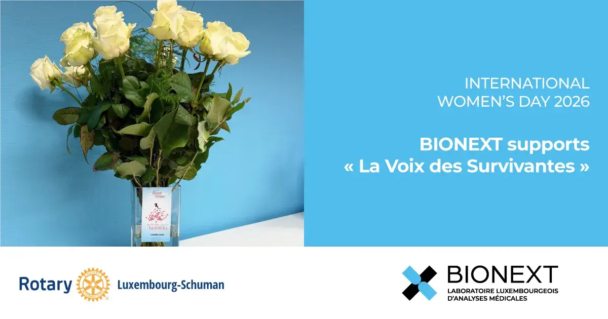 Bouquet of white roses in a vase displayed for International Women’s Day 2026 with the message “BIONEXT supports La Voix des Survivantes”, alongside the Rotary Club Luxembourg-Schuman.